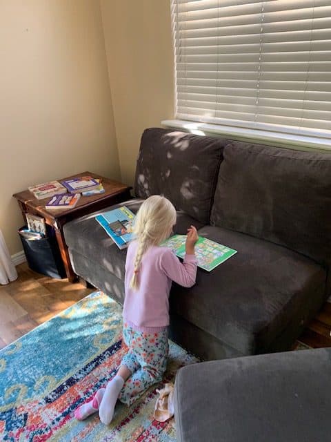 little girl exploring a book by a couch books available around the home